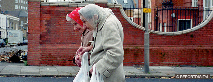 Two elderly white women walking, carrying plastic carriers, rubbish on street corner