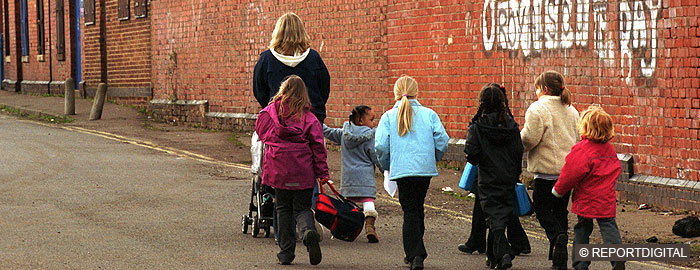 Woman with pushchair and seven children walking past graffitti, rear view, children of mixed