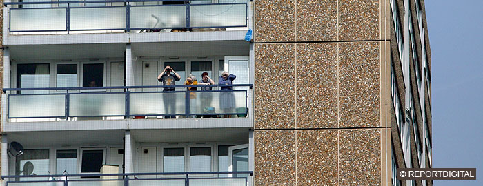 Four people, white, adults and children, looking out from high-rise balcony
