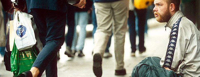 Man begging in street, people walking by