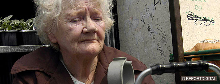 Elderly woman with crutches, looking distressed, graffiti on wall behind