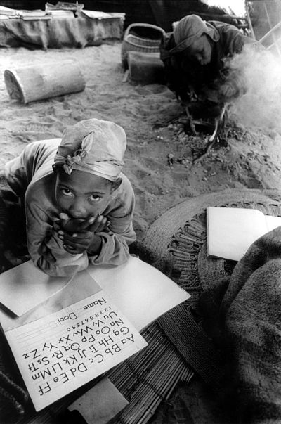 African girl writing alphabet, firelight, mother cooks