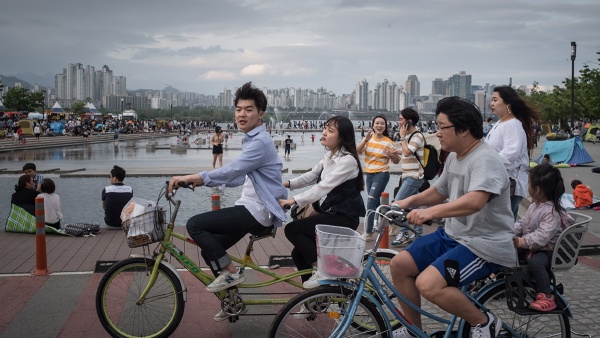 Youths and children riding bicylces in Yeouido Park Seoul with city in background. From cfr.org