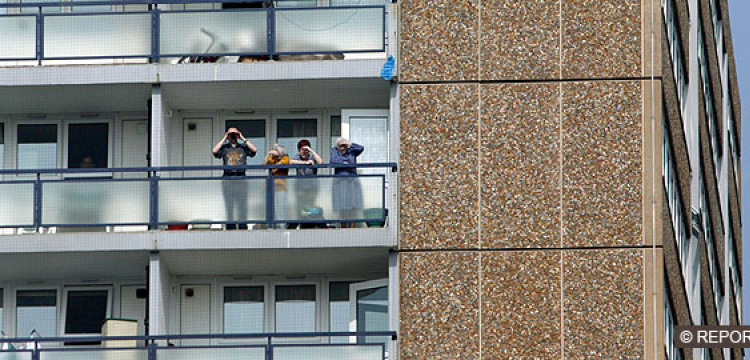 Four people, white, adults and children, looking out from high-rise balcony