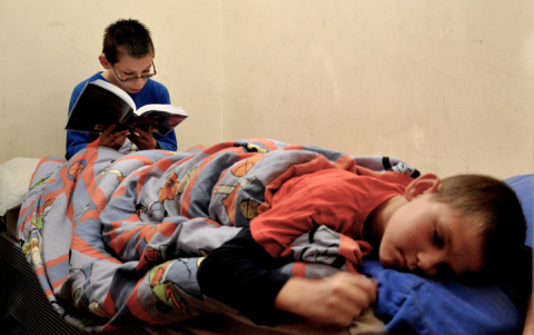 Two young boys, one reading, share beds 